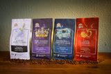Four standing coffee bags on a wooden surface with scattered coffee beans in front, photographed against a textured wall. The bags are labeled 'Lunar Veritasum', 'The Haem of Destiny', 'Pandora's Open Box', and 'Soul Stone', with Treasured Aromas branding visible.